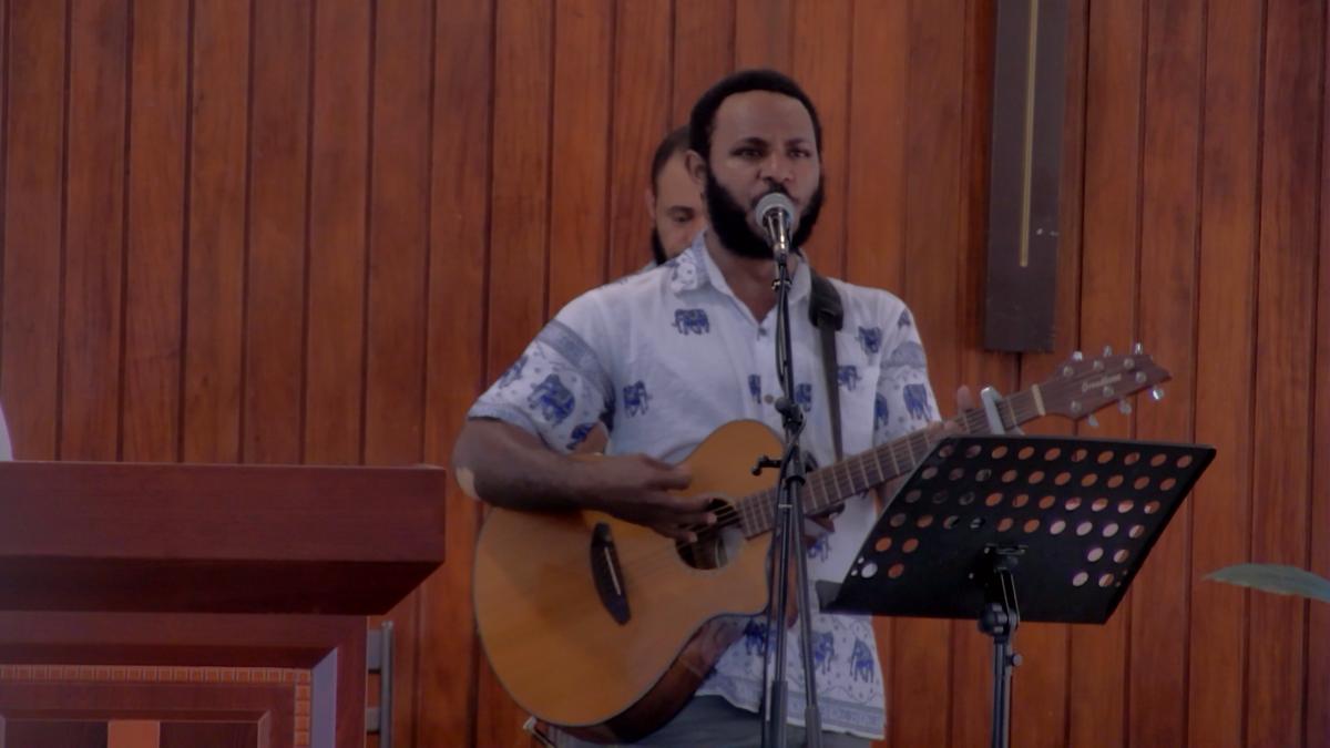 The worship leader with his guitar in front of the timber wall of the sanctuary